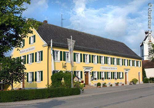 Ein langes dreistöckiges Gebäude im fränksichen Baustil mit gelber Fassade und grünen Fensterläden. Das Haus steht an einer geteerten Straße.