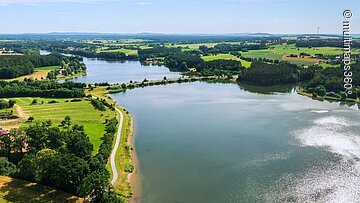 Luftbild von einem Teil des Rothsees. Der See ist umgeben von grünen Wiesen. Entlang des Ufers wachsen viele Bäume und Sträucher.
