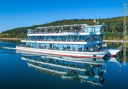 Die MS Brombachsee fährt über den See. Am Ufer grüne Bäume und Sträucher.