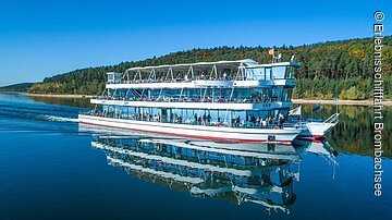 Die MS Brombachsee fährt über den See. Am Ufer grüne Bäume und Sträucher.