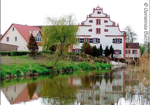 Eine große barocke Mühle an einem Weiher. Die Mühle spiegelt sich im Wasser.
