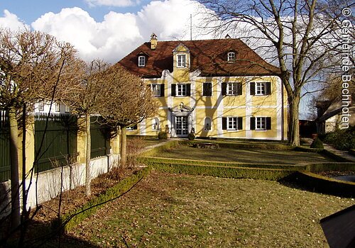 Ein Schloss im Barockstil mit weiß-gelber Fassade und grünen Fensterläden. Davor ein große Wiese.