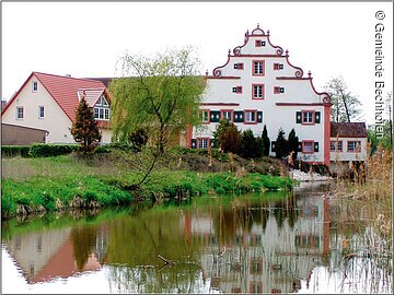 Eine große barocke Mühle an einem Weiher. Die Mühle spiegelt sich im Wasser.