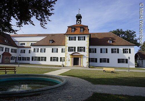 Frontansicht der markgräflichen Sommerresidenz Triesdorf. Ein barockes Schlößchen mit weißer Fassade und grünen Fensterläden.
