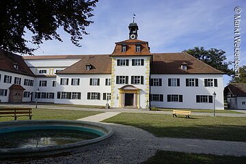 Frontansicht der markgräflichen Sommerresidenz Triesdorf. Ein barockes Schlößchen mit weißer Fassade und grünen Fensterläden.