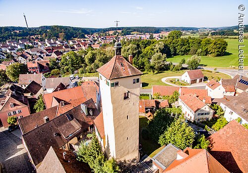 Luftbild  eines Stadtturms. Ein großer Turm mit beiger Fassade und rotem Ziegeldach. Um den Turm Häuserdächer.