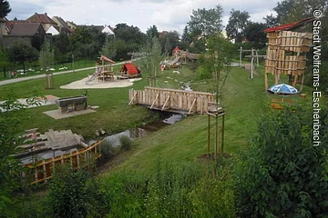 Vogelperspektive auf den Ritterspielplatz in Wolframs-Eschenbach mit vielen Spielgeräten, wie beispielsweise einem Turm. Der Spielplatz liegt auf einer grünen Wiese umgeben von Grün.