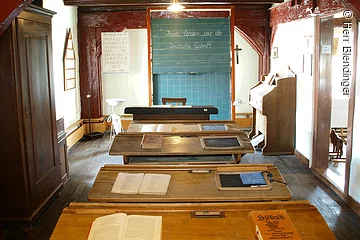 Ein alter Schulraum im Heimatmueseum Merkendorf. Ein Raum in welchem vier alte Schulbänke aus Holz hintereinander in einer Reihe stehen. Ganz vorne eine grüne Kreidetafel.