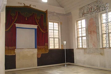 Innenraum einer Synagoge. Weiße Wände. Darauf ein roter gemalter Vorhang.