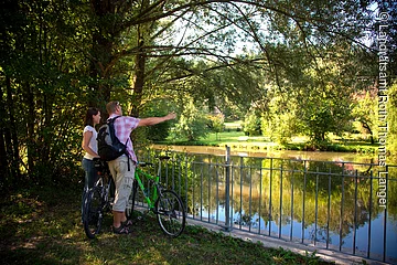 Am Flussufer der Roth in Eisenhammer genießen zwei Fahrradfahrer den einmaligen Ausblick auf die Roth. Die Roth ist an den Ufern umgeben von grünen Sträuchern und Bäumen.
