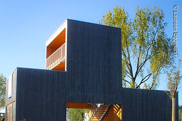 Ein offenes Gebäude mit Holzfassade in Form. Der Pavilion besteht aus drei Blöcken. Davor eine grüne Wiese.