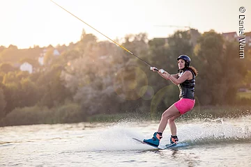 Eine junge Frau gleitet mit ihrem Wakeboard über den See.