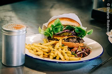 Ein Hamburger mit Pommes auf einem weißen Teller. Der Teller steht auf einer schwarzen Tischplatte.