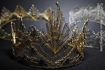 Eine geklöppelte goldenen Krone liegt auf einem grauen Untergrund.