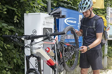 Ein Fahrradfahrer mit Helm repariert an einer Reparaturstation sein Hinterrad
