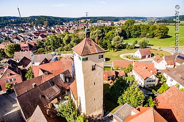 Luftbild  eines Stadtturms. Ein großer Turm mit beiger Fassade und rotem Ziegeldach. Um den Turm Häuserdächer.