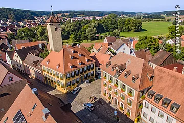 Luftbild der Altstadt Windsbach. Eine breit gepflasterte Straße an der Häuser im fränkischen Baustil stehen. Ein großer Stadtturm ragt über die Dächer hinweg.