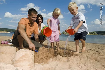 Eine vierköpfige Familie spielt am Strand des Brombachsees in Ramsberg. Die zwei Kinder erfreuen sich am sandeln und genießen die Zeit.