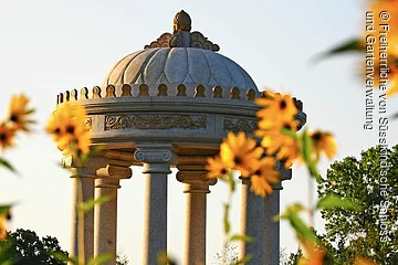 Fokus auf einen runden Steinpavillion im Schlosspark Dennenlohe. im Vordergrund gelbe Blumen.