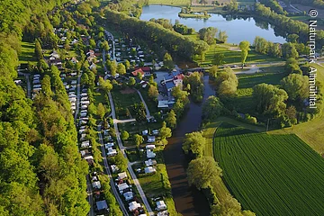 Der Campingplatz Kratzmühle mit vielen Wohnmobilen, -wagen von oben gesehen. Der Platz ist ein wenig in den Hang eingebettet und rechts ist schon der Kratzmühlsee.