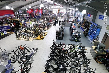 Blick von oben auf die Verkaufshalle eines Fahrradgeschäfts. In der Halle stehen viele Räder in Reihen.