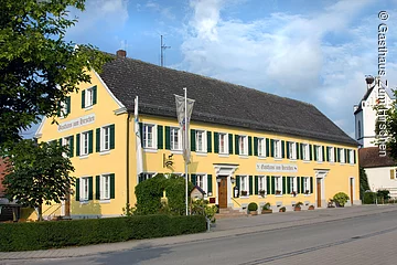 Ein langes dreistöckiges Gebäude im fränksichen Baustil mit gelber Fassade und grünen Fensterläden. Das Haus steht an einer geteerten Straße.