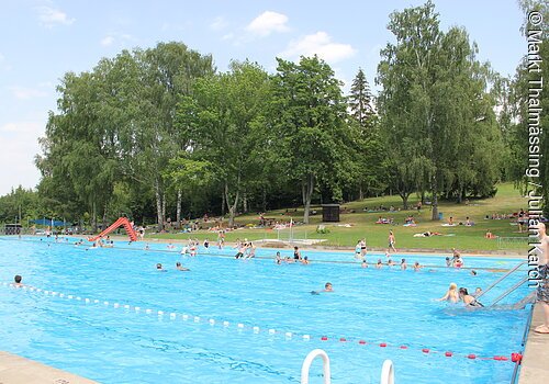 Im Schwimmerbecken tummeln sich einige Schwimmer. Ein paar Badegäste sonnen sich auf der Liegewiese.