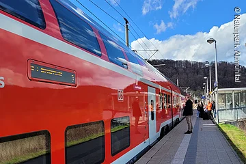 Eine Regionalbahn hat am Gleis gehalten und Reisende warten darauf, dass sich die Türen öffnen.