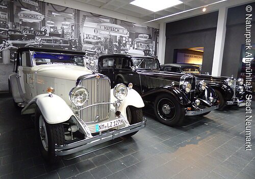 Drei Oldtimer-Autos nebeneinander in einem Museum mit historischem Schwarz-Weiß-Foto im Hintergrund.