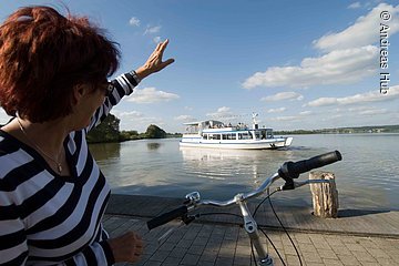 Eine Fahrradfahrerin grüßt die Passagiere der MS Altmühlsee vom Ufer aus